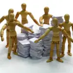 Picture of wooden people surrounding piles of documents